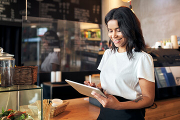 Happy waitress barista using digital tablet at work in cafe, restaurant - obrazy, fototapety, plakaty
