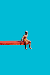 miniature man sitting on a red diving board