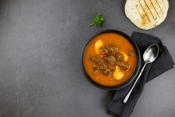 Hungarian goulash - beef meat stewed with potatoes, carrots, paprika, spices, flatbread on a gray background. Top view, copy space.