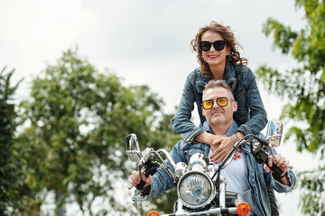 Fototapeta na wymiar Cool happy mature couple in demin jackets riding motorbike in city