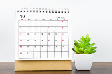 The October 2022 desk calendar with plant on wooden table.