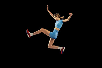 Fototapeta na wymiar Young sportive girl, long jumper in sports blue uniform performs triple jump isolated on black background. Concept of sport, energy, achievements, motion, speed.