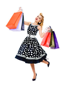 Full body of jumping, running, dancing woman in pinup style black dress holding, showing carrying shopping bags isolated on white background. Sales discounts rebates or consumer bank credit ad concept