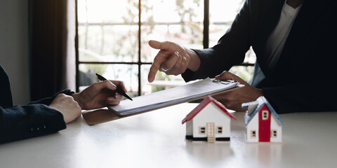 A real estate agent with a House model is talking to clients about buying home insurance. Home...