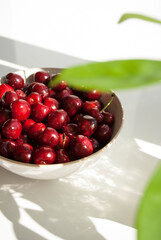 Red cherries on a plate with long shadows on white background. Fruit on a table. Vitamin healthy food