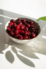 Red cherries on a plate with long shadows on white background. Fruit on a table. Vitamin healthy food