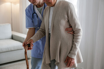 Senior woman with a cane getting assistance in elderly care facility. Hospital nurse taking care of...