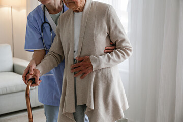 Senior woman with a cane getting assistance in elderly care facility. Hospital nurse taking care of...