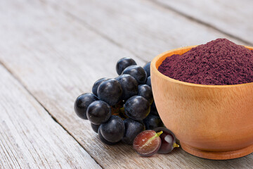 Grape extract flour (opc grape powder) in wooden bowl and fresh black grapes isolated on wooden...