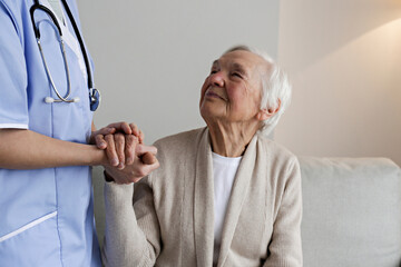 Portrait of older adult female in elderly care facility holding hands with a nurse. Senior woman...