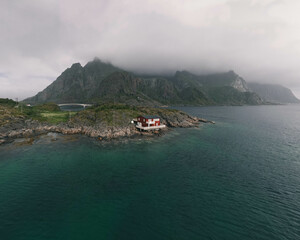 Red norwegian hut in front of the ocean with mountains and a bridge in the background