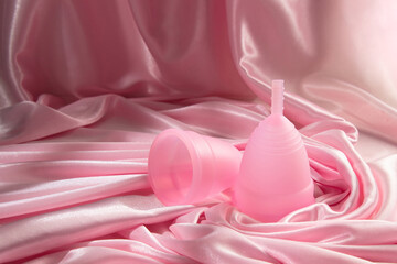 Two menstrual cups of different sizes made of medical silicone, against the background of delicate folds of pink silk and satin