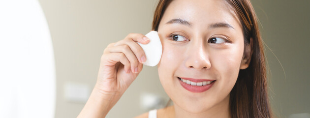 Happy asian woman looking at mirror and using cotton pad clean make up on her face © Pormezz