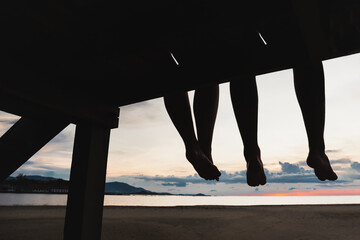 Fototapeta na wymiar Silhouette feet of couple sitting on the pier at sunset beach.