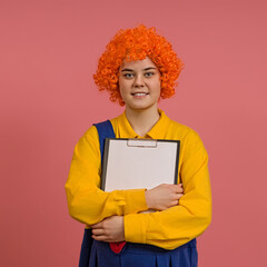 funny clown in a wig and a yellow-blue suit hugs a tablet with a clip on a colored background