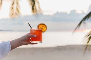 Female holding glass of cocktail on the beach at sunset.