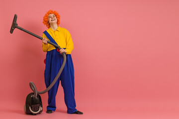young woman in a wig and a clown costume laughs and does cleaning with a vacuum cleaner on a...