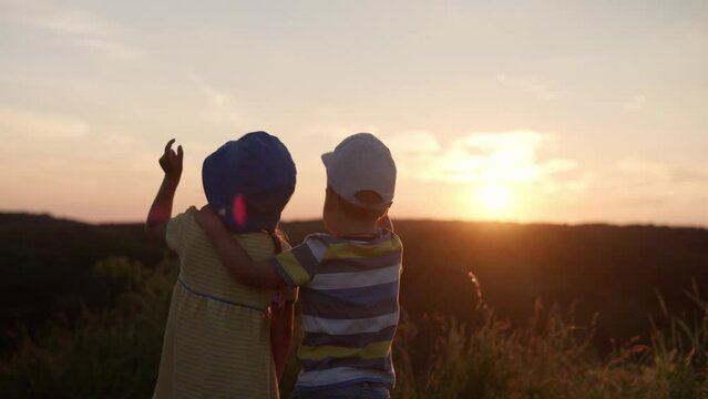 Cute Happy Preschool Baby Couple Hugging And Looking Into Distance On Top Of Mountain In Tall Grass Before Sunset. Child Walk In Field Meadow. Childhood, Nature, Lifestyle, Friendship, Summer Concept