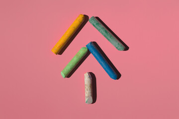 colored pastel crayons lie like a herringbone on a pink background