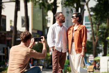 Young man photographing friends in park on sunny day