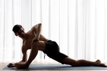 Young fit man doing yoga practice in studio in the morning