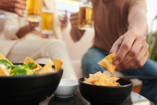 Close-up image of young people having corn chips while drinking beer in bar