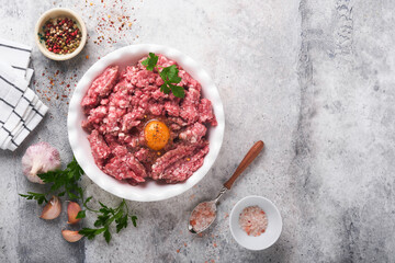 Raw minced meat. Ground meat beef, pork or lamb spices, herbs and eggs on white plate on light grey concrete background. Fresh minced meat ready for cooking. Food cooking background. Top view.
