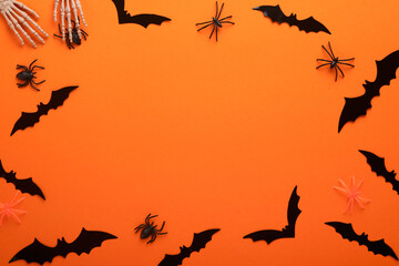 Orange Halloween background. Flock of black bats, spider, pumpkin, skeleton and leaves for Halloween. Black paper bat silhouettes on orange background. Autumn decoration. Halloween concept. Top view.