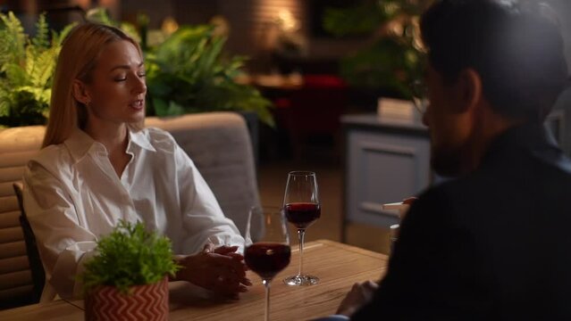 Happy young man and woman sitting at restaurant table using hand sanitizer before eating. Elegant male helping disinfect hands to blonde female during romantic dinner date. Shooting in slow motion.