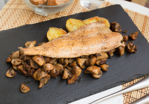 fried trout fillet on pillow of fried champignon mushrooms on dark warm stone plate