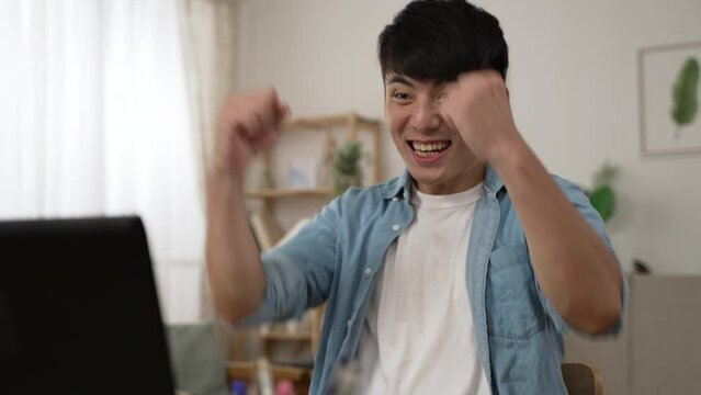 overjoyed asian businessman celebrating with yes hand gesture for receiving great business opportunity and replying email on laptop while working from home