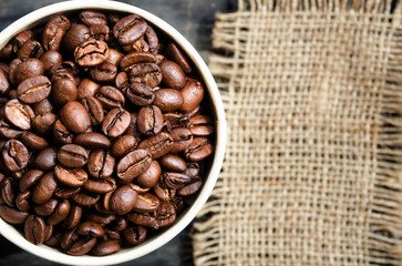 Fototapeta premium Coffee beans in a paper cup. Burlap in blur, space for text.