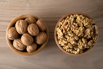 Bowl of walnuts and whole walnut kernels on wooden background,top view
