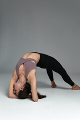 Happy healthy beautiful woman in comfortable sports clothes having fitness workout. Fit young lady in lilac crop top and yoga pants standing isolated on beige background and doing exercise