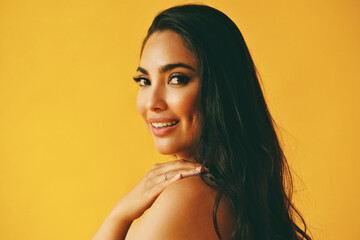 headshot beauty shot of hispanic Latina woman smiling young adult with hand on shoulder black long hair and tank top in front of yellow background looking at camera studio shot - obrazy, fototapety, plakaty
