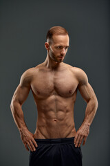 Fototapeta premium Young male athlete posing. Handsome athletic male power guy. Fitness muscular person. Young athlete showing muscles in the studio, posing shirtless on gray background.