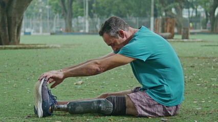 Athletic disabled person with prosthetic leg stretching at park