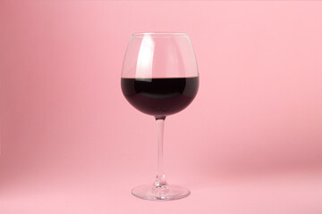 A glass of red wine on a pink background. Alcoholic drink.