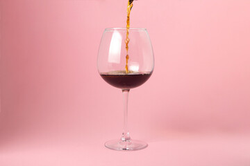 Red wine is poured into a glass on a pink background. Alcoholic drink.
