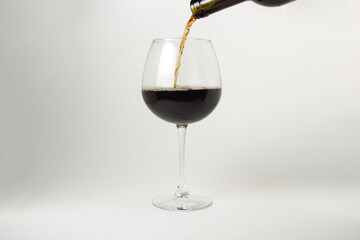 Red wine is poured into a glass on a white background. Alcoholic drink.