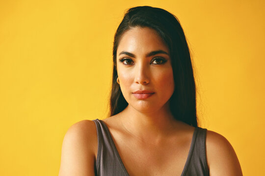 Headshot Beauty Shot Of Hispanic Latina Woman Thoughtful Young Adult With Black Long Hair And Tank Top In Front Of Yellow Background Looking At Camera Studio Shot