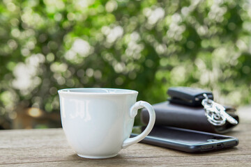 White cup coffee and wallet,key car and mobile on the wood table.