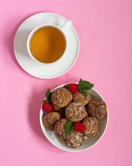 Gingerbread in a white bowl with raspberries, next to a mug of tea on a plate on a bright pink background. Vertical arrangement.