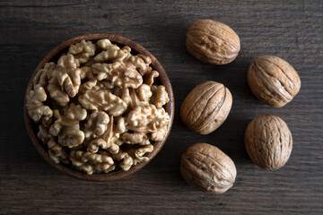 Bowl of walnuts and whole walnut kernels on wooden background,top view
