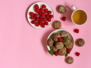 Gingerbread cookies in a white bowl with raspberries and tea and a plate with raspberries on a pink background, top view, free space
