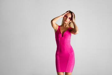 Front image of a sexy blonde female model in pink slim dress isolated on grey background. Space for...