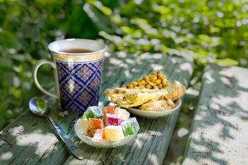 Oriental sweets lukum kozinaki halva and tea in a patterned cup among the greenery of nature on a sunny summer morning. Tea party in Oriental style.