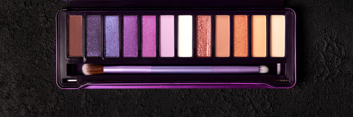 Colorful eye shadow palette on dark black background banner. Color eyeshadow palette with brush. Wide panoramic header