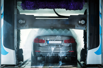 A grey business sedan vehicle running through an automatic car wash with brushes and water hitting...