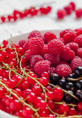 Raspberry close up, red and black currant in a white plate. Natural sweets.